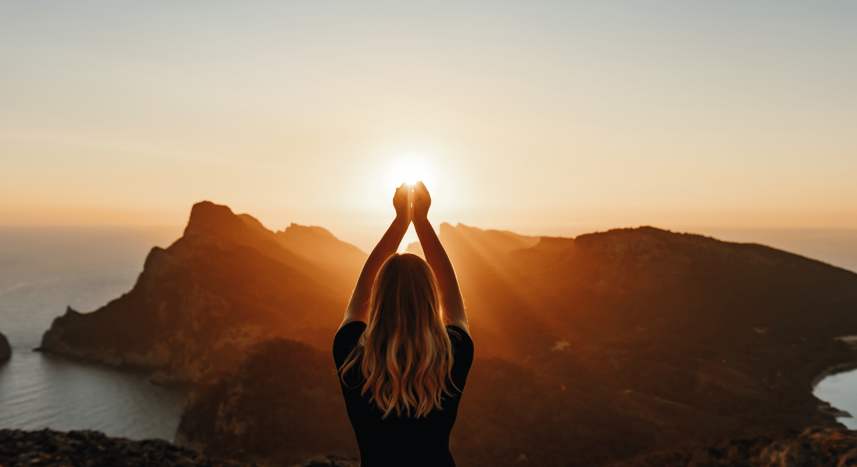 A woman facing the sea at sunrise